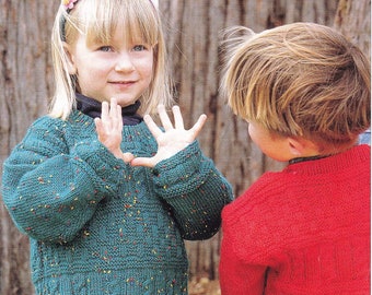 May include: Two children, one wearing a green jumper with a colourful flecked pattern and the other wearing a red jumper, stand facing each other. The child in the green jumper is holding out their hands, as if they are playing a game.