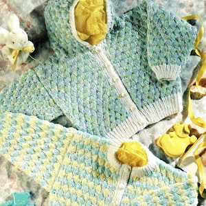 Op de afbeelding: Twee gebreide baby-vestjes in blauw, wit en geel. Het vestje bovenaan heeft een capuchon en is gemaakt met een textuur-steek. Het vestje onderaan heeft een eenvoudiger steekpatroon.