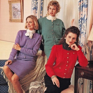 May include: Three women wearing cardigans. The woman on the left is wearing a purple cardigan and skirt. The woman in the middle is wearing a green cardigan and skirt. The woman on the right is wearing a red cardigan and black trousers.