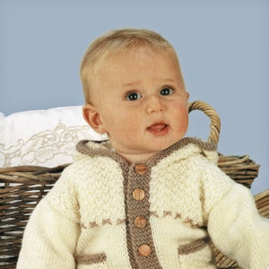 May include: A baby wearing a cream knitted cardigan with brown trim and wooden buttons. The cardigan has a hood and pockets. The baby is wearing brown corduroy pants and white socks.