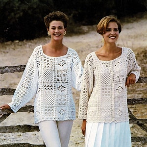 May include: Two women wearing white crocheted sweaters. One woman is wearing a white skirt and the other is wearing white pants. They are standing in front of a wooden fence.