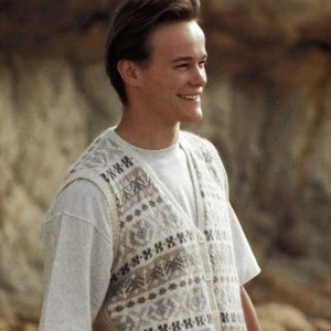 Può includere: Un gilet di maglia bianco con un motivo geometrico marrone e grigio. Il gilet ha una scollatura a V e una chiusura con bottoni.