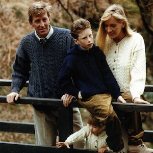 May include: A family of four wearing knitted sweaters stand on a wooden bridge. The father is wearing a blue sweater, the mother is wearing a white sweater, the son is wearing a dark blue sweater, and the daughter is wearing a white sweater.