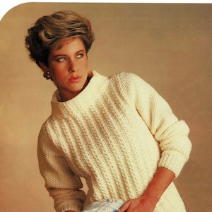Puede incluir: Primer plano de una mujer con un suéter de crochet blanco de cuello alto. Está sosteniendo una tela a cuadros en sus manos.