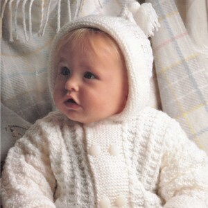 May include: A white knitted baby cardigan with a hood and matching mittens. The cardigan has a button closure and a cable knit pattern.
