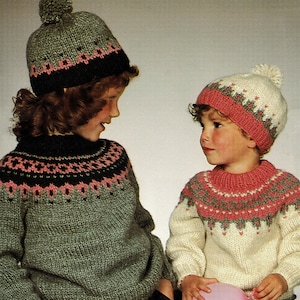 May include: Two children wearing knitted sweaters and hats. The child on the left is wearing a green sweater with a black and pink pattern and a green hat with a black and pink pattern. The child on the right is wearing a white sweater with a pink and grey pattern and a white hat with a pink and grey pattern. The child on the right is holding a pink balloon.