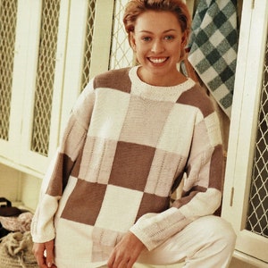 Op de afbeelding: Een vrouw draagt een witte en bruine geruite trui met een witte broek en witte schoenen.