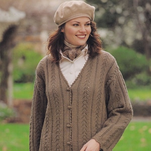 May include: A brown knitted cardigan with a V-neck and button closure. The cardigan has a lace pattern and a scalloped hem. The model is wearing a white shirt and a brown scarf.