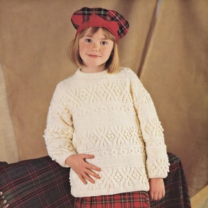 May include: A young person wearing a white knitted sweater with a cable knit pattern and a red and black plaid skirt. They are also wearing a red and black plaid beret.
