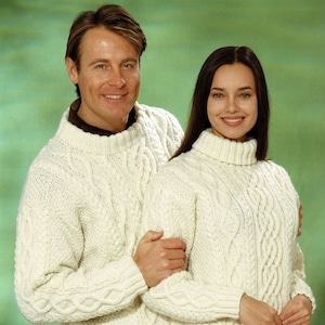 Könnte beinhalten: Zwei weiße Strickpullover mit Zopfmuster, einer mit Rollkragen und der andere mit Rundhalsausschnitt.