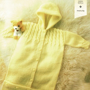 May include: A yellow knitted baby sleeping bag with a hood and button closure. The sleeping bag is laid out on a white fluffy surface. The text "SIZES 40/45cm Sleeping Bag" is visible in the top right corner of the image.