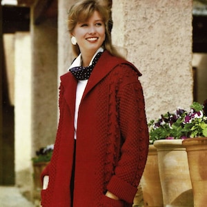 Könnte beinhalten: Ein langer, roter Strickmantel mit strukturiertem Muster und großen Taschen. Der Mantel hat einen Schalkragen und wird über einem weißen Hemd und einer schwarzen Hose getragen. Die Mantellänge beträgt ca. 122 cm.