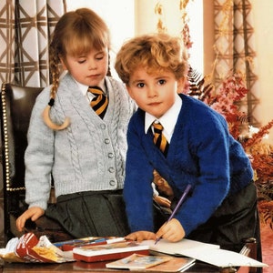 May include: Two children wearing school uniforms are sitting at a table. The girl is wearing a light blue sweater with a cable knit pattern and a black skirt. The boy is wearing a blue sweater with a cable knit pattern and black pants. They are both wearing white shirts with a yellow and black striped tie. The girl is holding a pencil and the boy is writing in a notebook.