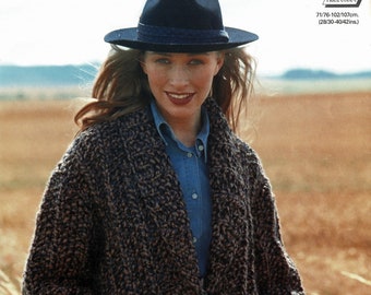 May include: A brown and black knitted cardigan with a button fastening and two pockets. The cardigan is being worn by a person wearing a blue shirt and a black hat.
