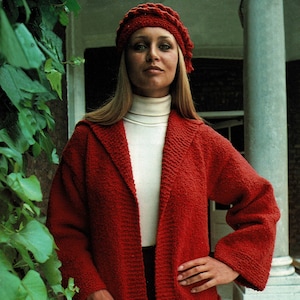 May include: A red knitted cardigan with a shawl collar and pockets. The cardigan is open in the front and has long sleeves. The model is wearing a white turtleneck sweater underneath.