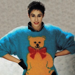 May include: A blue fuzzy sweater with a yellow teddy bear wearing a red bow tie on the front.