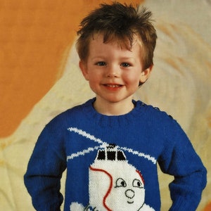 Könnte beinhalten: Ein blauer Strickpullover mit einem weißen Hubschrauber-Design. Der Hubschrauber hat einen roten Streifen und ein lächelndes Gesicht.