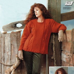 May include: A red knitted sweater with a cable knit pattern and a round neckline. The sweater is worn by a person with long red hair and is paired with dark green pants and brown boots. The image also shows a close-up of a second red sweater with a v-neck.