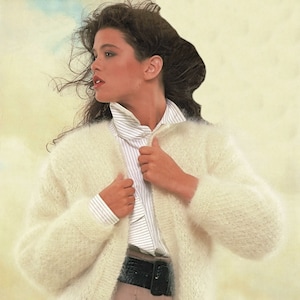 May include: A white fuzzy cardigan with a button closure. The cardigan is worn over a striped white shirt and brown pants with a black belt.