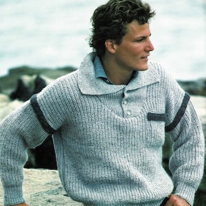 May include: A light grey knitted jumper with dark grey trim on the sleeves and collar. The jumper has a button closure at the neck.