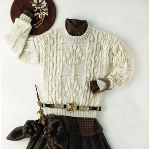 May include: A white knitted sweater with a cable knit pattern, a brown plaid shirt, a brown belt with a gold buckle, and a brown skirt.