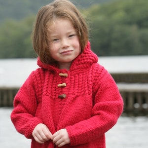 May include: A red knitted hooded jacket with wooden toggle closures. The jacket has a cable knit pattern and is being worn by a young child.