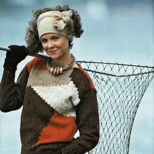 May include: A woman wearing a brown and white patterned sweater with a beige headband and a beaded necklace is holding a fishing net with fish inside.