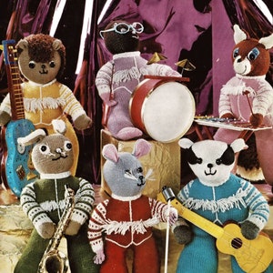 Puede incluir: Un grupo de siete figuras de animales de punto, vestidos con trajes coloridos, cada uno tocando un instrumento musical. La banda incluye un oso con una guitarra, un topo con un tambor, un ciervo con un xilófono, un tejón con un ukelele, un conejo con un saxofón y un ratón con un micrófono.