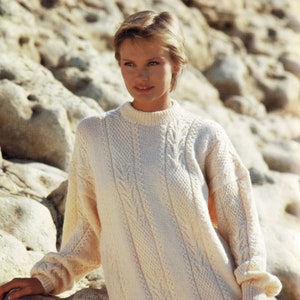 May include: A white knitted sweater with a cable knit pattern. The sweater has a round neckline and long sleeves.