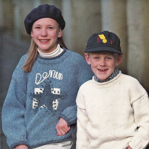 Puede incluir: Dos niños con suéteres de punto. La niña lleva un suéter azul con una estrella blanca y la palabra "denim" en él. También lleva una boina azul. El niño lleva un suéter blanco y una gorra de béisbol negra con un logotipo amarillo y rojo.