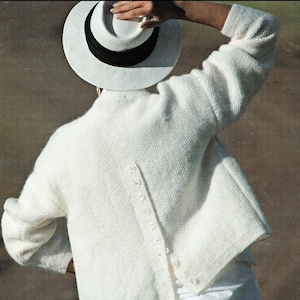 Puede incluir: Un cárdigan blanco de lana de cordero con cierre de botones en la espalda. El cárdigan está tejido en punto fino y tiene un corte holgado.