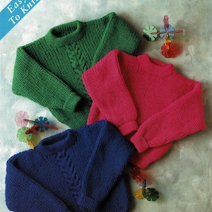 May include: Three knitted sweaters in green, pink, and blue with a cable knit design. The sweaters are laid out on a light brown surface. The text "Easy To Knit" is in a blue box in the upper left corner of the image.