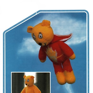 May include: A knitted orange teddy bear wearing a red cape with a yellow flame design. The bear is flying in the air with a cloud behind it. The caption below the image reads "Double Knitting".