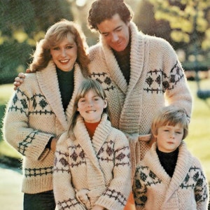 May include: A family of four wearing matching cream knitted cardigans with a geometric pattern. The cardigans have a shawl collar and a tie belt. The family are standing in a park setting.