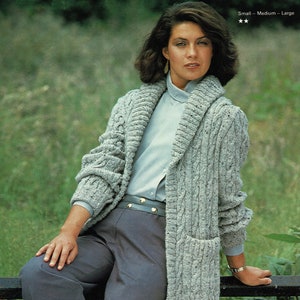 May include: A long, gray cable knit cardigan with a large collar and a patch pocket. The cardigan is worn over a light blue button-down shirt and gray pants.