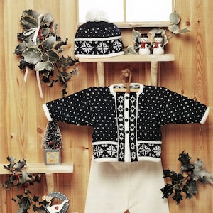 Può includere: Un completo in maglia per neonato in bianco e nero con un motivo a fiocco di neve. Il completo comprende un cappello, un cardigan, pantaloni e scarpine. Il completo è esposto su uno sfondo in legno con rami di agrifoglio.