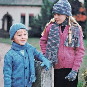 Puede incluir: Dos niños con cardigans, gorros y bufandas de punto a juego. La niña lleva un cardigan rosa con una bufanda blanca y azul, y el niño lleva un cardigan azul con una bufanda azul. Ambos niños llevan guantes a juego.