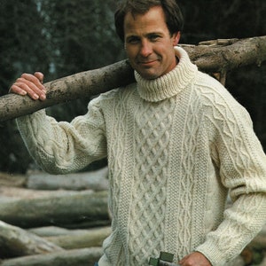 May include: A cream-colored cable knit sweater with a high turtleneck. The sweater is made of a thick yarn and has a relaxed fit. The model is wearing the sweater with blue jeans and is holding a wooden log over their shoulder.