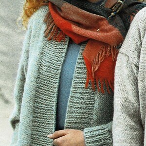 May include: A woman wearing a grey knitted cardigan with a red and blue scarf. The scarf has a decorative pin with blue and gold accents.