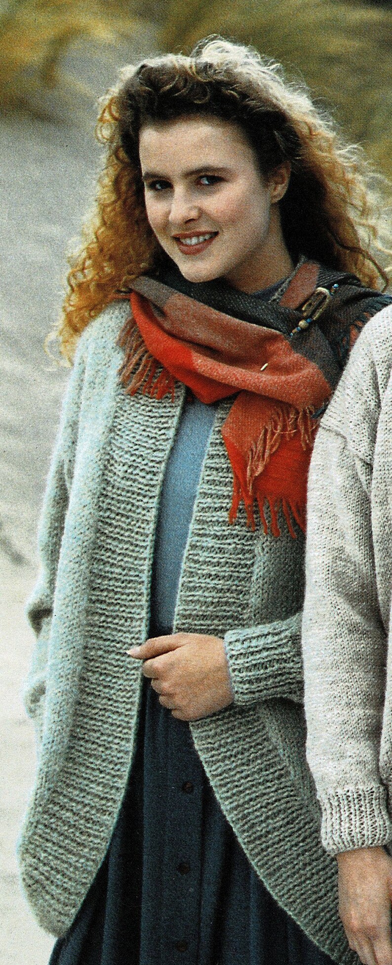 May include: A woman wearing a grey knitted cardigan with a red and blue scarf. The scarf has a decorative pin with blue and gold accents.
