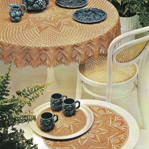 May include: A brown crocheted tablecloth with a starburst design covers a white table with a blue and white ceramic pitcher and bowl. Two blue and white ceramic plates are on the table. A white chair with a woven cane seat is next to the table. A brown crocheted doily is on a white table with four blue and white ceramic cups.