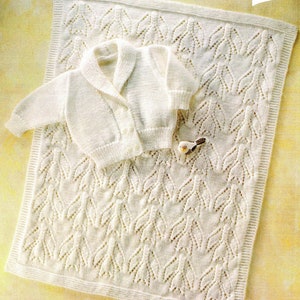 May include: A cream-colored, knitted baby blanket and matching jacket. The blanket features a repeating leaf pattern, and the jacket has a shawl collar and button closure. A small decorative bird is placed on the blanket. The size of the blanket is 51cm.