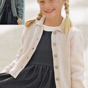 May include: A young girl wearing a light pink knitted cardigan with a collared neckline and button closure. She is wearing a black dress underneath the cardigan. The cardigan has a textured knit pattern and is buttoned up the front.