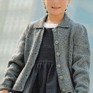 May include: A young person wearing a gray knitted cardigan with a dark gray dress underneath. The cardigan has a button-up front and a collared neckline.