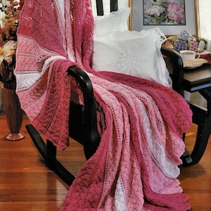 May include: A pink and white crocheted throw blanket draped over a rocking chair. The blanket has a gradient pattern of pink and white stripes.