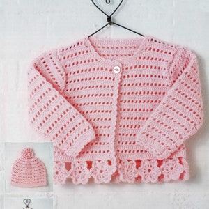 May include: A pink crocheted cardigan with a button closure and a scalloped hem. The cardigan is hanging on a heart-shaped hanger. There is a matching pink crocheted hat in the image.