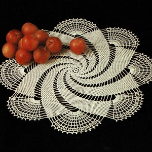 Puede incluir: Un encaje de ganchillo blanco con un diseño en espiral. El encaje está decorado con un grupo de manzanas rojas.