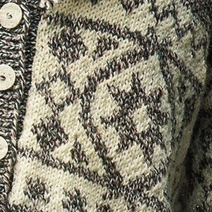 May include: Close-up of a knitted cardigan with a brown and white geometric pattern. The cardigan has a button closure and a fringe trim.