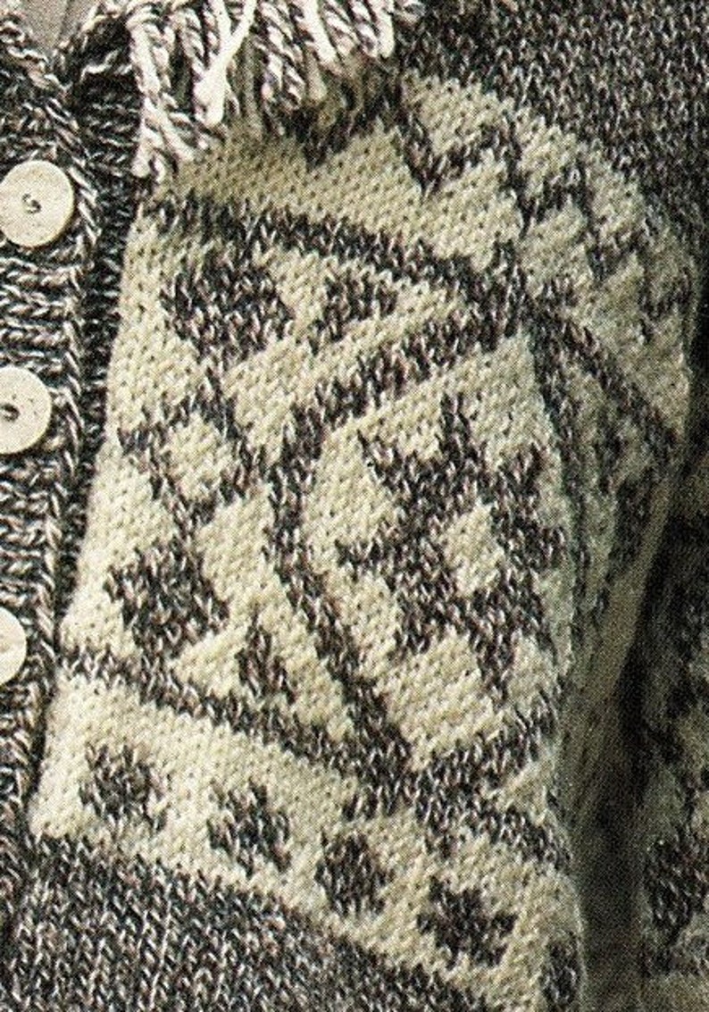 May include: Close-up of a knitted cardigan with a brown and white geometric pattern. The cardigan has a button closure and a fringe trim.