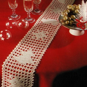 Könnte beinhalten: Ein weißer gehäkelter Tischläufer mit einem zarten Muster auf einer roten Tischdecke. Der Läufer liegt auf einem Tisch mit drei Gläsern Champagner und einer Schale Trauben.